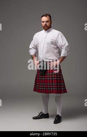Schottischer Rotschopf-Mann in rotem Kilt auf grauem Hintergrund Stockfoto