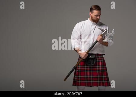Schottischer Rotschopf-Mann in rotem Kilt mit Schlachtaxt auf grauem Hintergrund Stockfoto