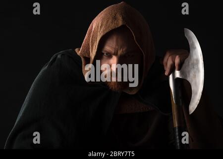 Porträt des runzelnenden mittelalterlichen schottischen Kriegers mit Schlachtaxt im Mantel auf schwarz isoliert Stockfoto