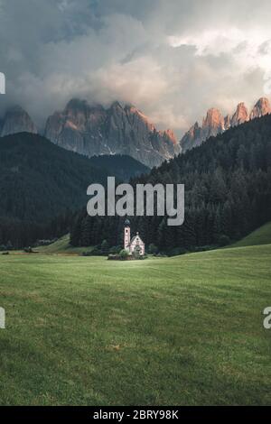 Panoramalicht auf die Kapelle St. Johann (San Giovanni auf Italienisch) in Ranui/Val di Funes mit der DolomitenGeisler-Gruppe im Hintergrund. Wunderschöner Sonnenuntergang in Sou Stockfoto