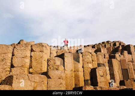 Ein Tourist in roter Jacke genießt das UNESCO-Weltkulturerbe Giants Causeway in Nordirland, das jetzt vom National Trust verwaltet wird. Stockfoto