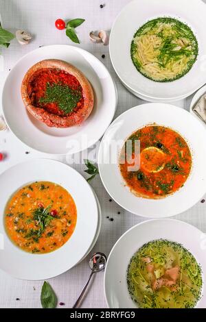 Variation von leckeren Restaurant warme Speisen Suppen flach legen. Draufsicht auf weißem Holztisch mit verschiedenen Suppen. Weltweite Küche, gesunde Ernährung, Stockfoto