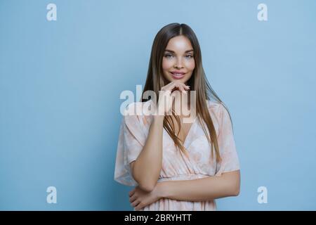 Taille up Schuss von ziemlich brünette Europäerin trägt stilvolle Sommerkleid, hält die Hände teilweise gekreuzt, hält Kinn, Gespräche mit Kollegen, isoliert über b Stockfoto