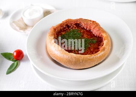 Russischer traditioneller Borsch im Brot mit Roggenbrot, Gewürzen und Kräutern auf hellem Hintergrund Stockfoto