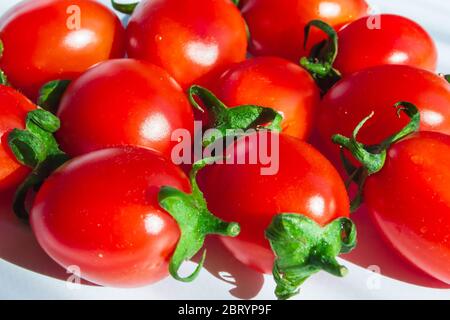 Frische kleine Kirschtomaten mit grünem Stiel auf hellem Hintergrund. Nahaufnahme. Selektiver Fokus Stockfoto