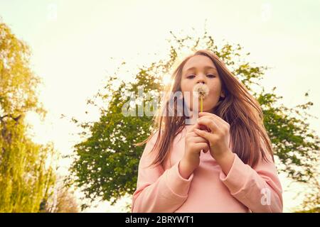 Portrait von lächelndes Mädchen mit langen Brünette Haare im Freien stehen, weht Löwenzahn. Stockfoto