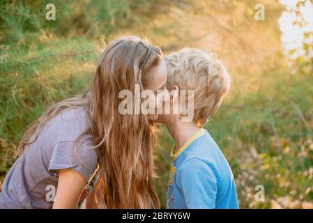 Junge und Mädchen knieten in einem Garten, flüstern einander ins Ohr. Stockfoto