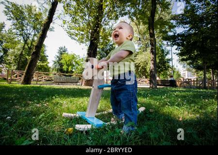 Porträt von Baby Mädchen spielen mit Schaukelpferd auf einem Rasen in einem Park. Stockfoto