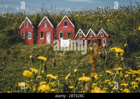 Trio von kleinen roten Elfen Häuser Hulduf lk mit Rasendächern in Island. Grünes Gras mit gelben Blüten. Stockfoto