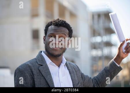 Porträt des lächelnden jungen Mannes mit kurzen Haaren in weißem Hemd und grauer Jacke, Blick auf die Kamera. Stockfoto