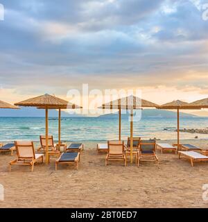 Malerischer Blick auf den Strand mit Reihen von Strohschirmen am Meer bei Sonnenuntergang Stockfoto