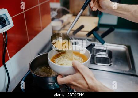 Hochwinkelaufnahme des Küchenchefs, der eine Schüssel mit Ramen-Noodle-Suppe in einem Ramen- und Gyoza-Restaurant in Italien zubereitet. Stockfoto