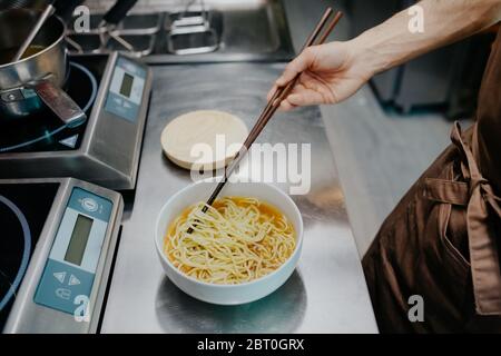 Hochwinkelaufnahme des Küchenchefs, der eine Schüssel mit Ramen-Noodle-Suppe in einem Ramen- und Gyoza-Restaurant in Italien zubereitet. Stockfoto
