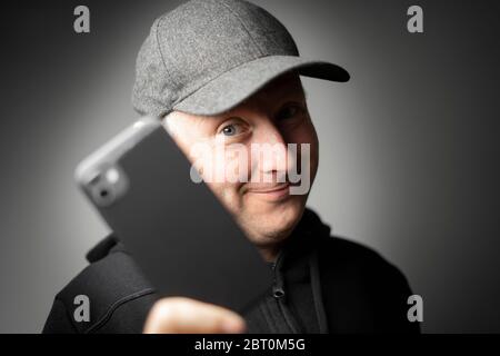 Content Mann in schwarzer Kleidung zeigt Smartphone an die Kamera Stockfoto