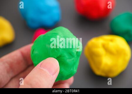 Mann mit grünen spielen Tonkugel in der Hand gegen bunte Plastilin-Kugeln. Nahaufnahme. Stockfoto