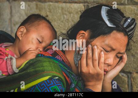 Die junge Mutter H'mong macht ein Nickerchen und trägt das Baby auf ihrem Rücken in Sapa, Vietnam. Stockfoto