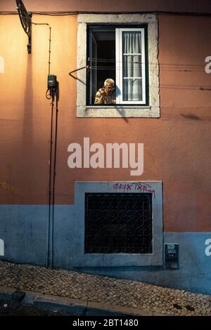 Europa, Portugal, Lissabon. Ein Mann schaut nachts aus seinem Fenster in den Straßen von Lissabon. Stockfoto