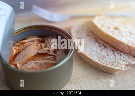 Nahaufnahme von offenem Thunfisch in Rotöl, Gabel und Brot auf Holztisch, Draufsicht Stockfoto