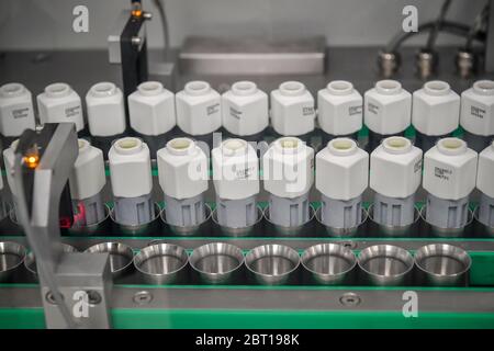 Flaschen, die ein Covid-19-Reagenz für Antikörpertestsätze enthalten, werden an der Produktionslinie des Ortho Clinical Diagnostics (OCD)-Testlabors in Pencoed in Wales mit Roboterarmen hinter Perspex-Abschirmungen entlang eines Förderers bewegt. Stockfoto