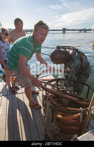 Tallinn, Estland - 18. Juli 2009: Ein Taucher im Tiefseeanzug kriecht aus dem Wasser. Ein Mann faltet einen Luftschlauch für Sauerstoff. Vertikal. Stockfoto