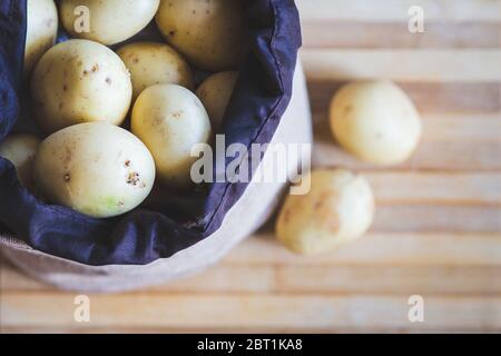 Rohe Kartoffelgerichte. Frische Kartoffeln in einem alten Sack auf Holzhintergrund. Draufsicht Stockfoto