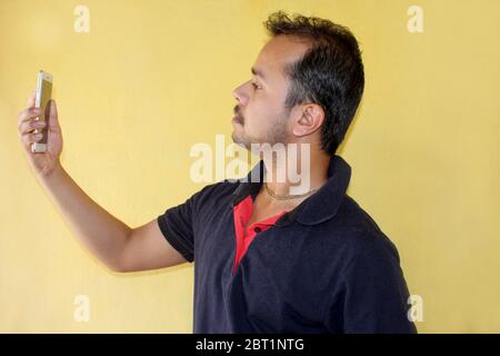 Junge schöne indische Mann unter Selfie mit Handy auf gelbem Hintergrund Stockfoto