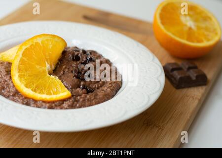 Eine Schüssel mit gesunden Frühstück Schokolade Orange Haferbrei Haferbrei Haferbrei mit Schokolade Chips und Kokosflocken darauf bestreut. Stockfoto