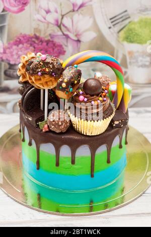 Blau-grüner Kuchen mit geschmolzener Schokolade, Kuchenschnaps, Lutscher, Donuts und Mini-Cupcakes. Stockfoto