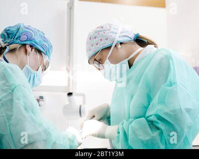 Frauen in Masken und sauber einheitliche Durchführung Heilverfahren auf Patienten während der Arbeit im Büro in modernen Zahnklinik Stockfoto