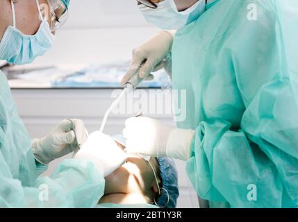 Von unten Zahnärzte in Uniform mit professionellen Werkzeugen, um Chirurgie auf anonymen Patienten während der Arbeit in der modernen Klinik zu tun Stockfoto