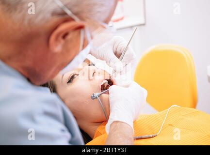 Erwachsener Mann mit professionellen zahnärztlichen Werkzeugen, um Zähne der jungen Dame während der Arbeit in der modernen Klinik zu heilen Stockfoto
