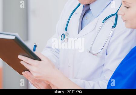 Nahaufnahme Von Männlichen Arzt Unterzeichnung Von Patienten Entlassung Papiere Von Weiblichen Krankenschwester Im Krankenhaus Gehalten. Stockfoto