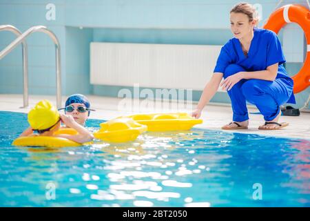 Kaukasische Weibliche Physiotherapeutin Führung Zwei Junge Patienten Während Der Schwimmbadrehabilitation Sitzung. Stockfoto