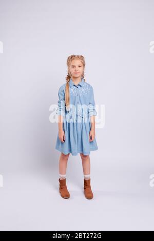 Langhaarige Mädchen steht auf einem hellgrauen Hintergrund in einem blauen Kleid. Stockfoto