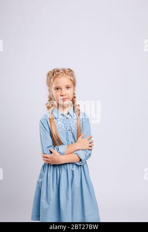 Langhaarige Mädchen steht auf einem hellgrauen Hintergrund in einem blauen Kleid. Stockfoto