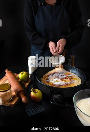 Traditionelle holländische Pfannkuchen mit Äpfeln auf der elektrischen Eisenpfanne auf schwarzem Hintergrund. Stockfoto