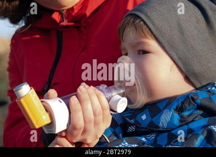 Ein kleiner Junge, der an Krankheit leidet Asthma bronchiale bekommen Behandlung mit Aerosol-Inhalator im Freien Stockfoto