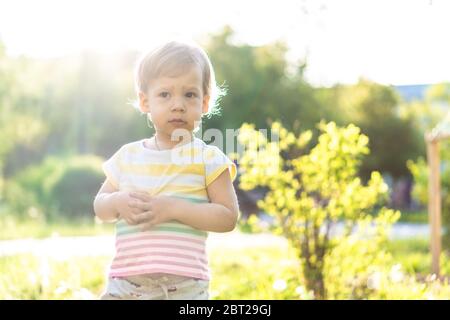 Kindheit, Natur, Sommer, Parks und Outdoor-Konzept - Porträt von niedlichen blonden kleinen Jungen in gestreiften mehrfarbigen T-Shirt mit serous, traurig Stockfoto