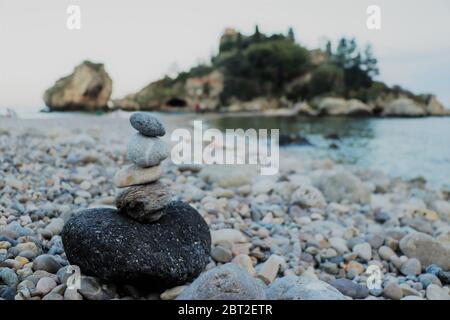 Steinhaufen, die am Strand entlang der Isola Bella, in der Nähe von Taormina, Sizilien, aufeinander balanciert sind. Italien Stockfoto