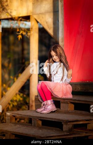 Kleines Mädchen aalen in den Strahlen der untergehenden Sonne sitzen auf einer Holztreppe Stockfoto