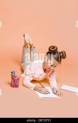 Girl liegt auf dem Bauch auf dem Boden und zieht mit Filzstiften in das Album Stockfoto