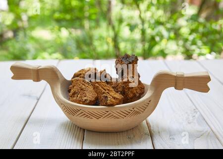 Chaga Pilz Scheiben liegt in einem Holzteller auf einem Holzhintergrund mit Wald Unschärfe Stockfoto