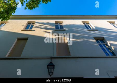 Niedrige Winkelansicht einer hellbeigen Fassade mit Außenlaterne und Laub, die Schatten wirft, Butte-aux-Cailles, Paris, Frankreich Stockfoto