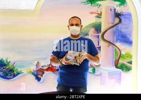 Ein junger Maler, der mit einer Tafel in der Hand porträtiert wurde, mit einem Gemälde einer Panoramaszene der Göttlichen Küste in seinem Atelier der bildenden Kunst Stockfoto