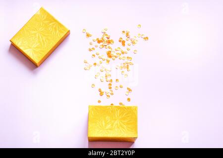 Gelbe offene Geschenkbox mit verschiedenen Party Konfetti auf rosa Hintergrund. Farbenfrohes Festkonzept. Flaches Lay. Stockfoto
