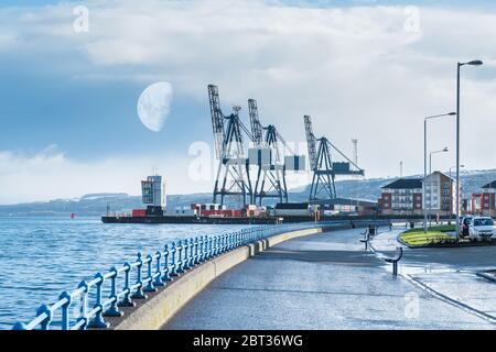 Greenocks Esplanade im westlichen Teil der Stadt mit Blick auf den kontrastierenden ClydePort Terminal mit Hafen und schweren Kranen. Früh morgens halb Stockfoto