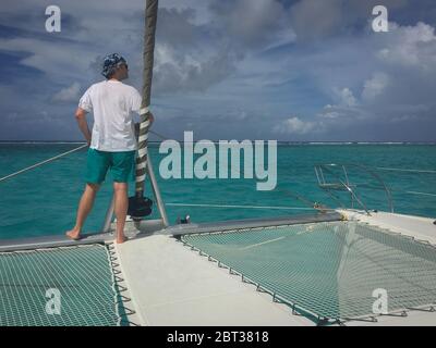 Ein reifer Mann, allein auf dem Deck eines Katamaransegel, der die weite Aussicht hat. Gesellschaft Inseln, Französisch Polynesien. Modellversion. Stockfoto
