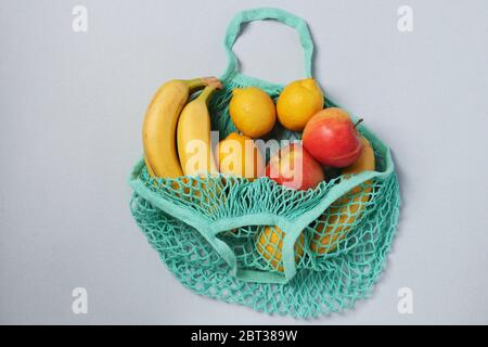 Gelbe reife Bananen, Zitronen und Äpfel in wiederverwendbaren String Mesh Bag türkis Farbe auf hellem Hintergrund, Zero Waste Konzept, Flat Lay Stockfoto