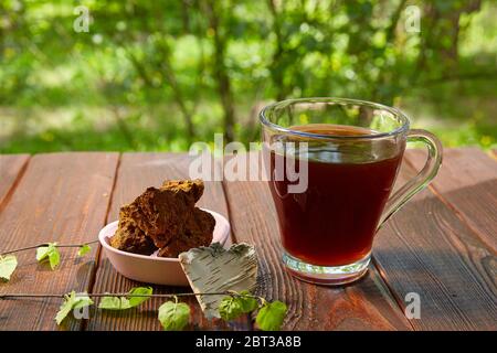 Tasse Chaga-Tee auf einem dunklen Tisch. Chaga-Pilzscheiben und ein Birkenzweig. Stockfoto