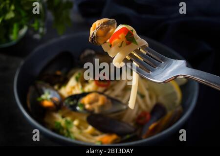 Gedämpfte Muscheln in Linguine Pasta in Weißweinsauce mit Knoblauch, Petersilie und rotem Chili in einem blauen Teller auf einem stimmungsvollen dunkelblauen Hintergrund. Selektiv f Stockfoto